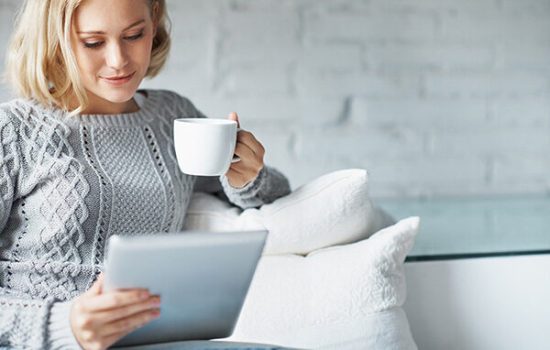 A pretty young woman using a digital tablet while enjoying a cup of coffee